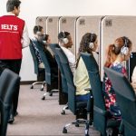 A group of test takers sat in booths with headphones on, sitting IELTS on computers.