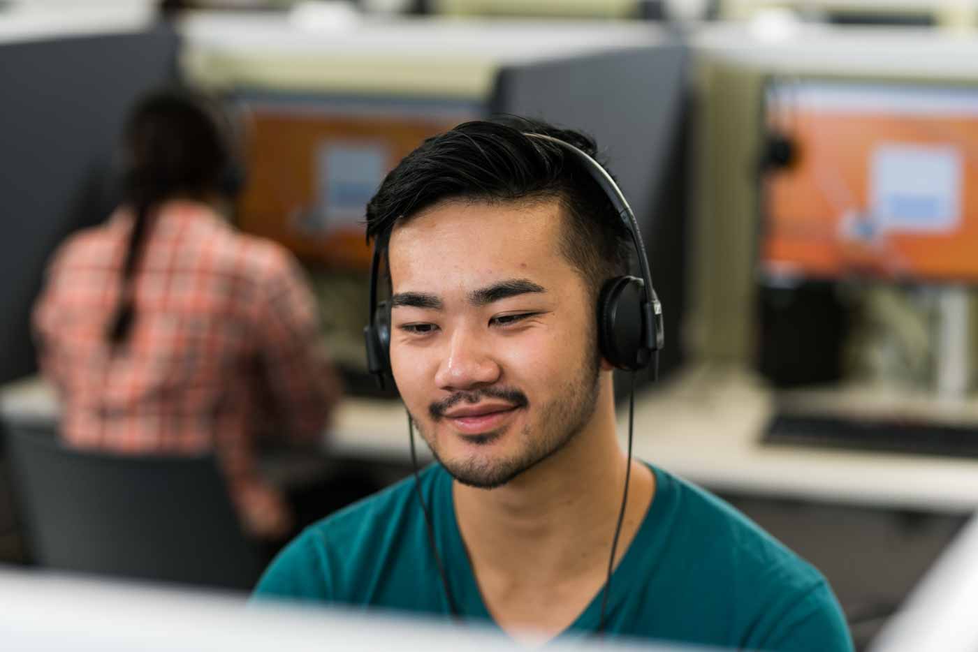 Man with headphones on sitting his IELTS test on a computer.
